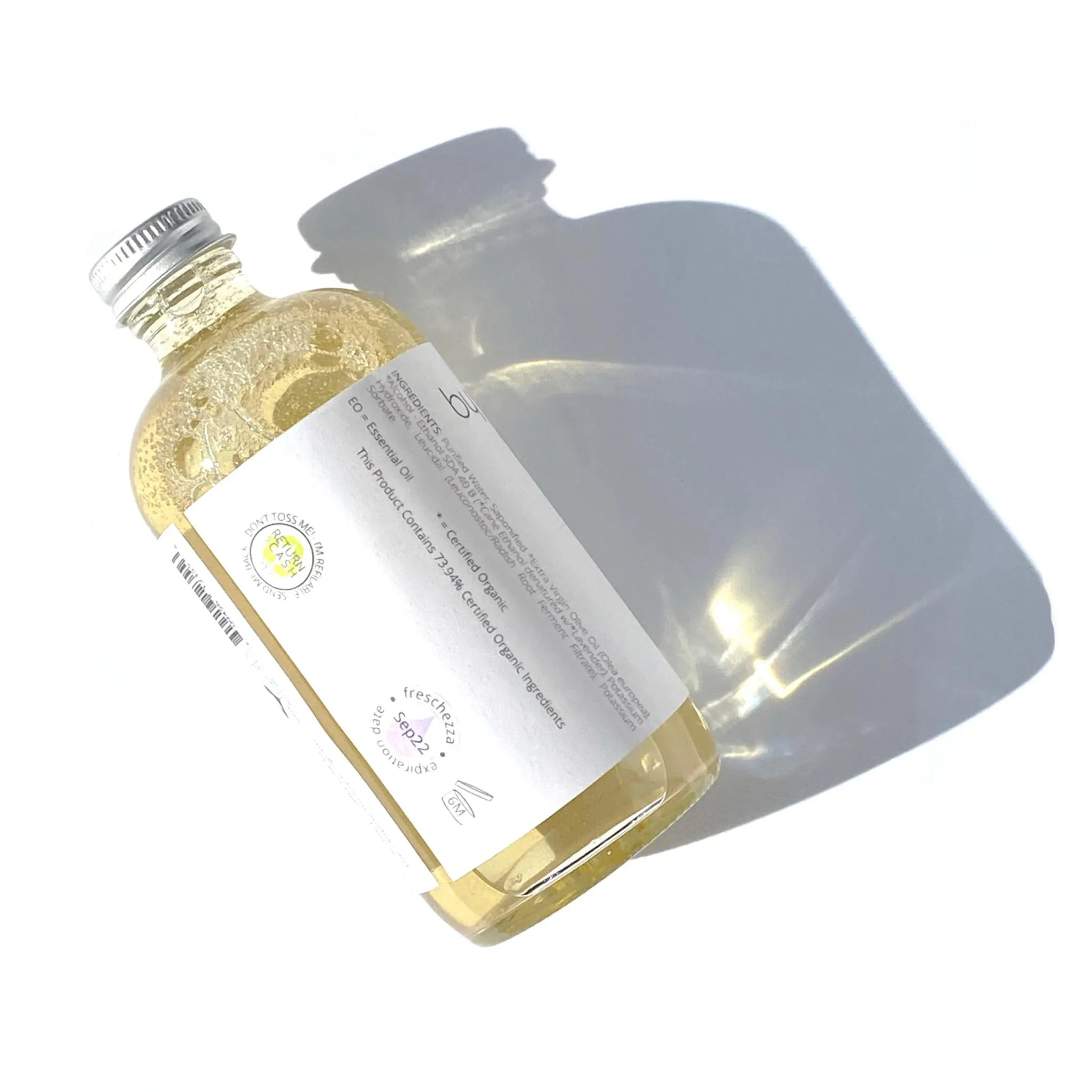 By Valenti Pure and Authentic Liquid Castile Soap in a glass bottle with a finger on the pump dripping soap, on a white background