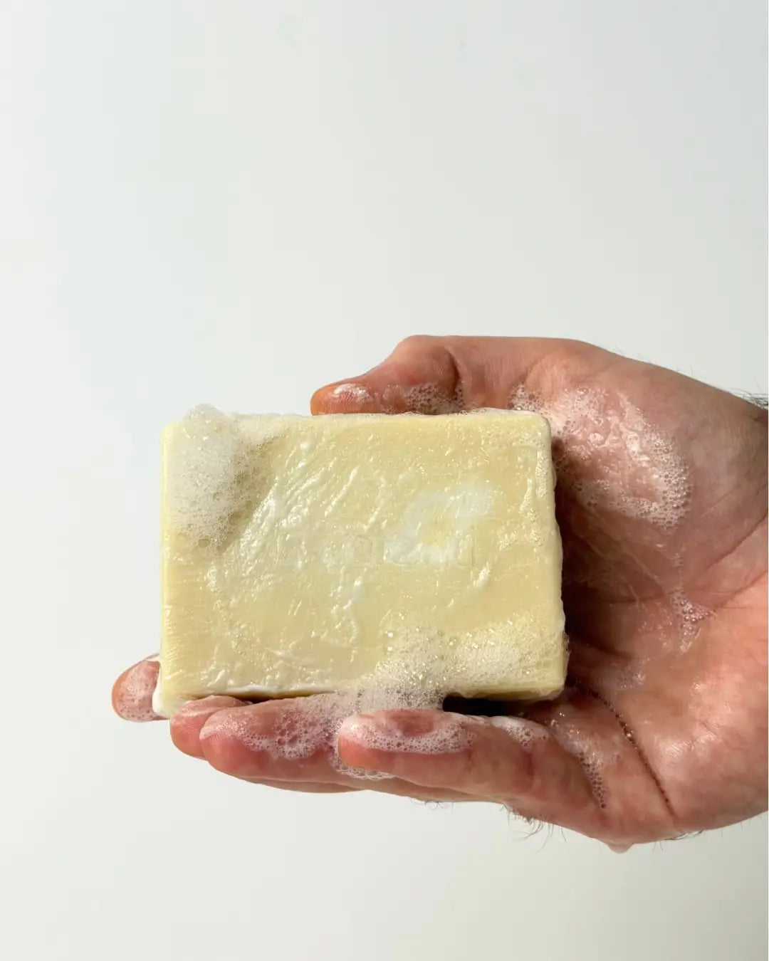 Hand holding a By Valenti Pure Castile bar soaps with lather on a white background
