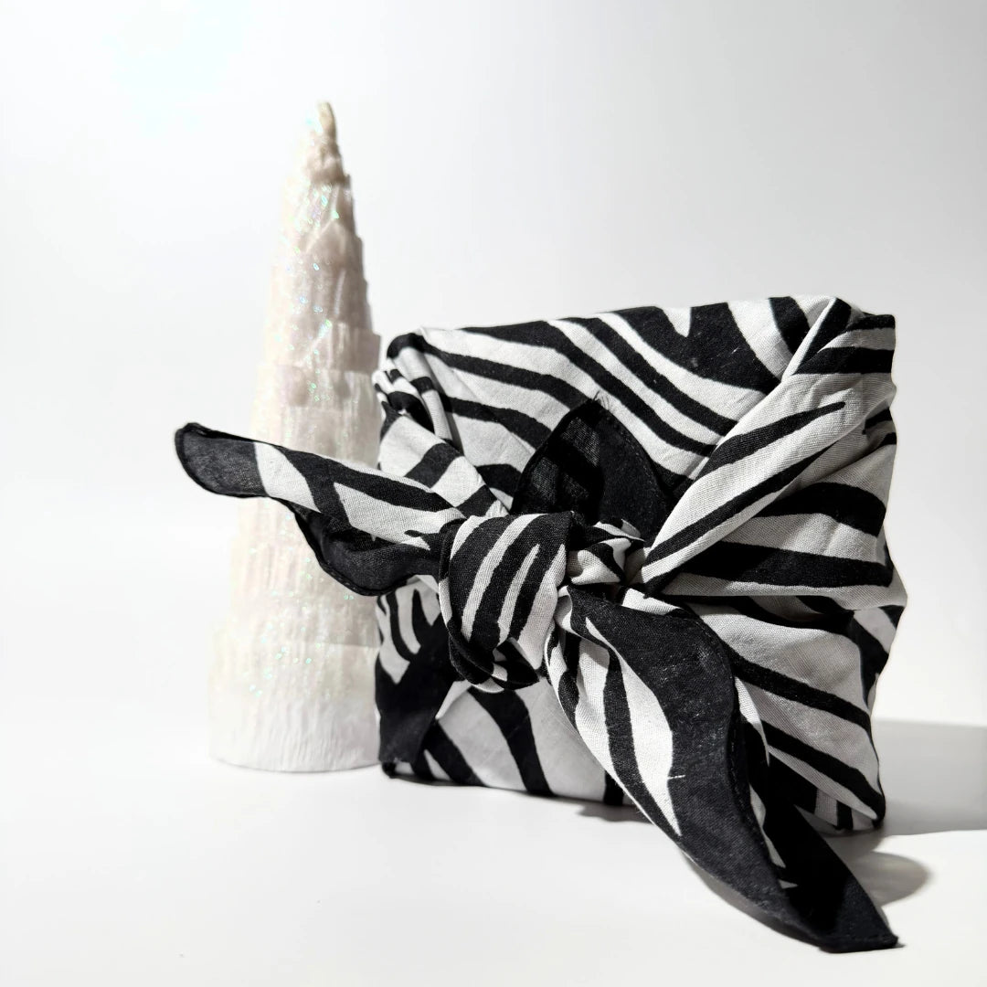 By Valenti black and white striped furoshiki wrapped gift box around a Christmas tree on a white background