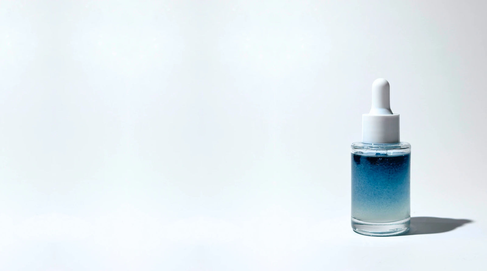 Skincare dropper bottle with blue gradient By Valenti bi-phase brightening serum on a white background